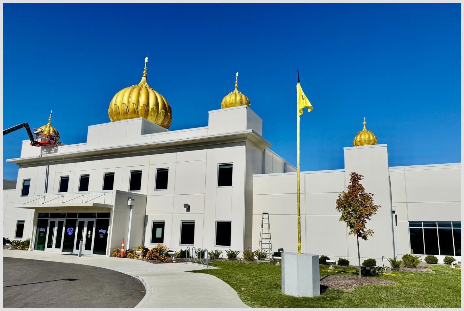 Full view of Gurdwara Sahib facade with installed golden Gumbad domes and manicured lawn in Indianapolis Indiana